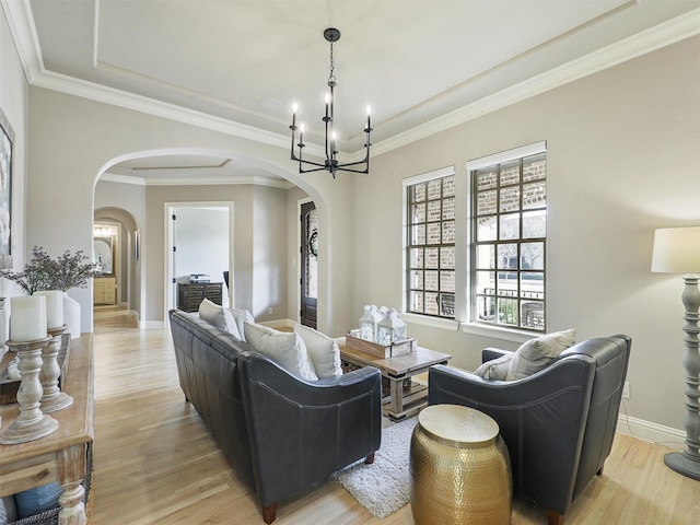 living room with light wood finished floors, baseboards, arched walkways, ornamental molding, and a notable chandelier