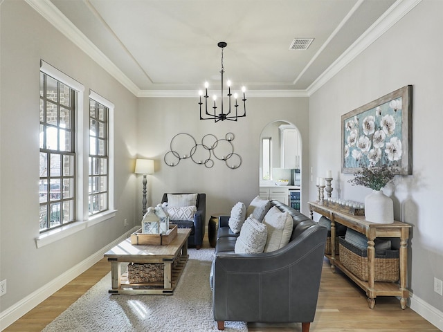 living area featuring arched walkways, baseboards, light wood-style flooring, ornamental molding, and a chandelier