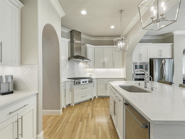 kitchen with arched walkways, stainless steel appliances, white cabinetry, light countertops, and wall chimney range hood