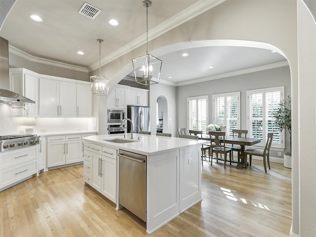 kitchen with arched walkways, visible vents, stainless steel appliances, light wood-style floors, and a sink