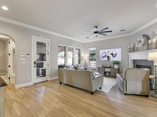 living area with visible vents, arched walkways, a tiled fireplace, ceiling fan, and light wood-style flooring