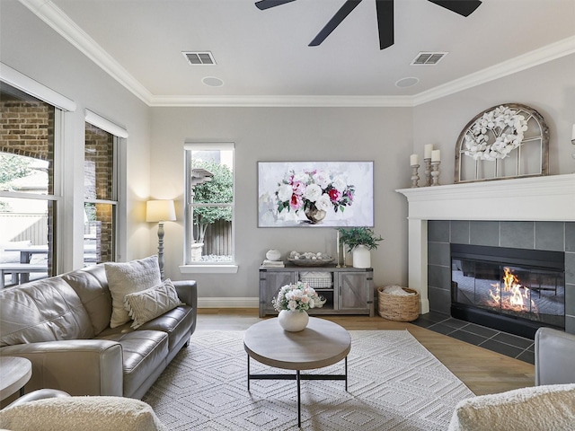 living area featuring ornamental molding, a tile fireplace, visible vents, and wood finished floors