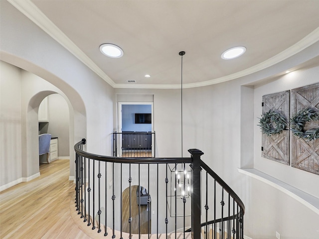 hall with light wood-type flooring, ornamental molding, arched walkways, and an upstairs landing