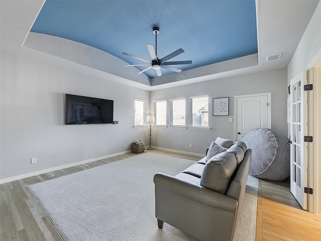 living room featuring light wood-style flooring, baseboards, and a raised ceiling