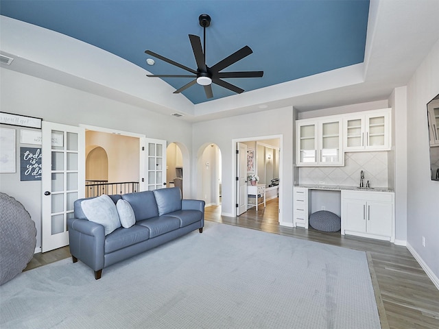 living room featuring visible vents, arched walkways, baseboards, dark wood-style floors, and a tray ceiling