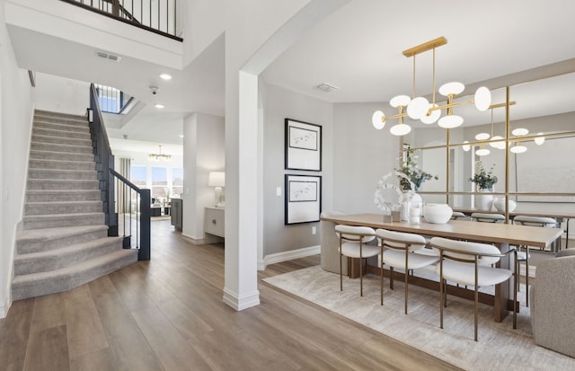 dining room with a notable chandelier, wood finished floors, visible vents, baseboards, and stairs