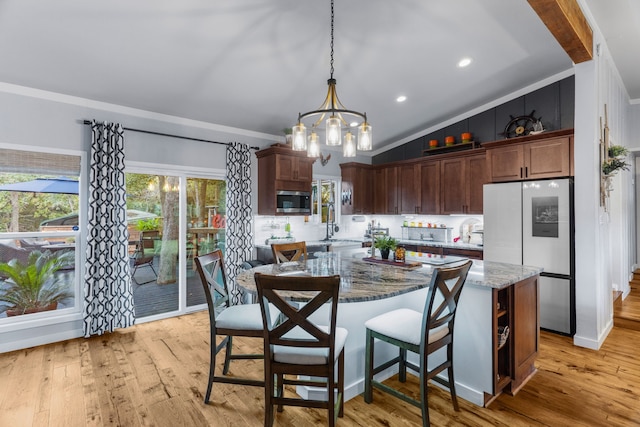 kitchen with lofted ceiling, light wood-style flooring, stainless steel appliances, a kitchen island, and light stone countertops