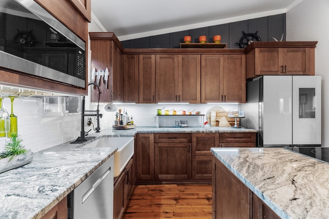 kitchen featuring stainless steel appliances, light stone countertops, backsplash, and wood finished floors