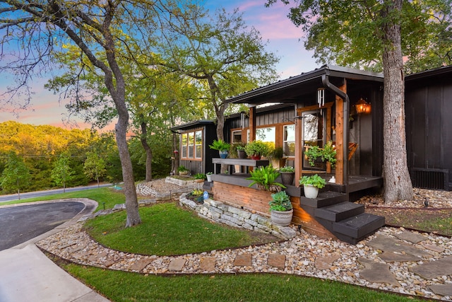 exterior entry at dusk featuring board and batten siding and a lawn