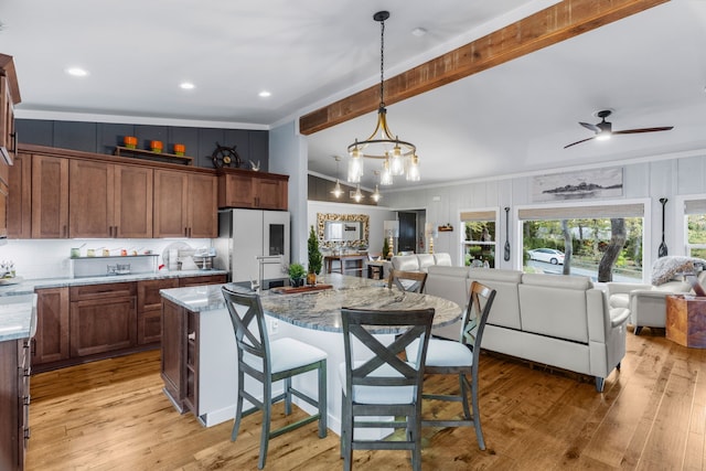 kitchen featuring a breakfast bar area, freestanding refrigerator, open floor plan, an island with sink, and light wood-type flooring