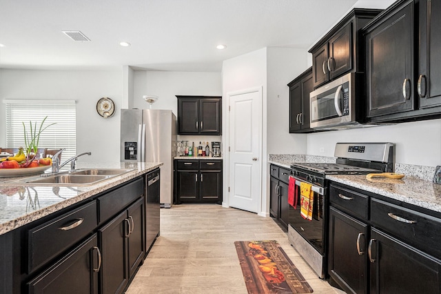 kitchen with appliances with stainless steel finishes, a sink, visible vents, and dark cabinets