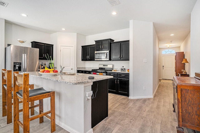 kitchen featuring dark cabinets, stainless steel appliances, a breakfast bar, a sink, and light wood-type flooring