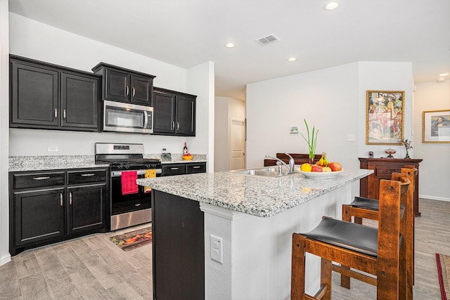 kitchen with dark cabinets, light wood-style flooring, stainless steel appliances, and a sink