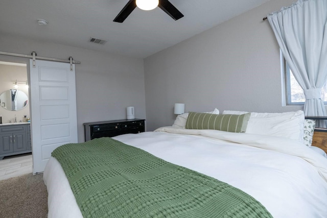 bedroom with a barn door, visible vents, a ceiling fan, connected bathroom, and a sink