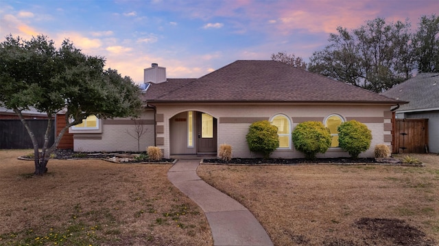 ranch-style home featuring brick siding, a lawn, a chimney, and fence