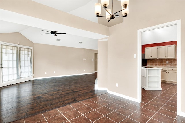 empty room featuring lofted ceiling, baseboards, dark tile patterned flooring, and ceiling fan with notable chandelier