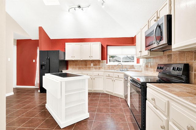 kitchen featuring vaulted ceiling with skylight, a sink, dark tile patterned floors, and black appliances