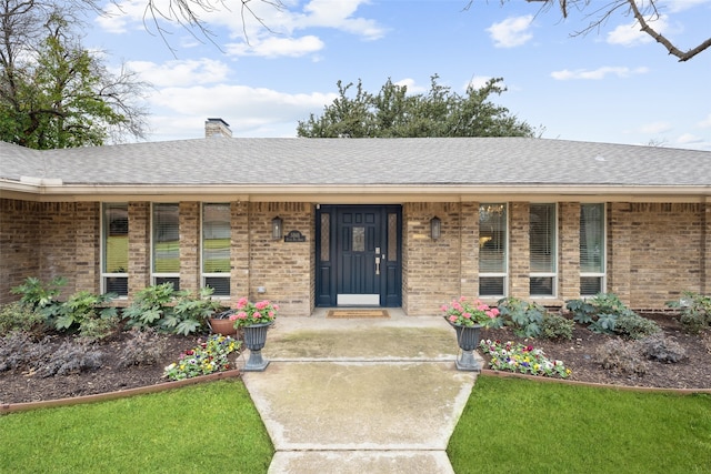 property entrance featuring roof with shingles, brick siding, a chimney, and a porch