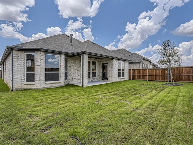 back of house with roof with shingles, brick siding, a patio, a lawn, and fence