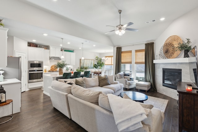 living area featuring lofted ceiling, a tiled fireplace, dark wood-style floors, and visible vents