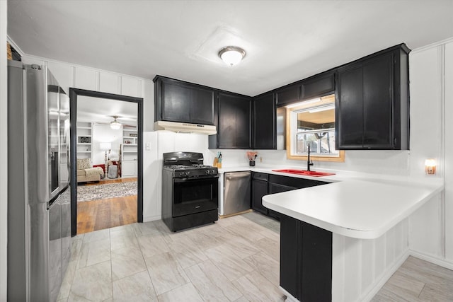 kitchen featuring light countertops, appliances with stainless steel finishes, a sink, dark cabinetry, and a peninsula