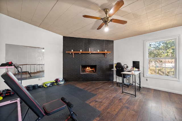 workout room with a brick fireplace, wood-type flooring, baseboards, and ceiling fan