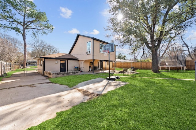 back of house with a gate, a trampoline, fence, and a lawn