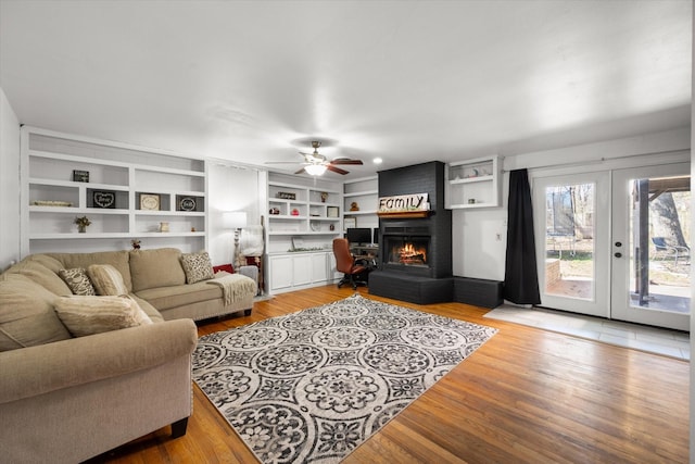 living room with light wood-style floors, ceiling fan, a fireplace, and french doors