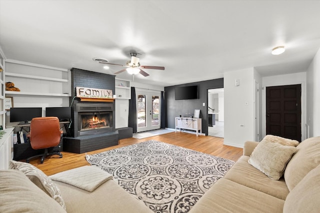 living room with wood finished floors, baseboards, built in features, french doors, and a brick fireplace