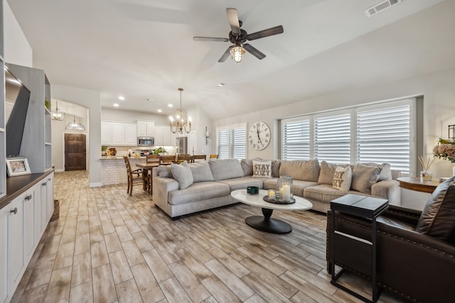 living room featuring lofted ceiling, light wood finished floors, visible vents, and ceiling fan with notable chandelier