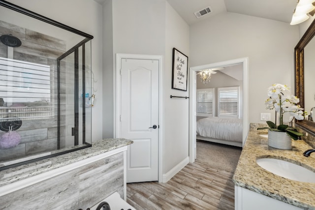 ensuite bathroom featuring lofted ceiling, visible vents, a stall shower, a sink, and wood finished floors