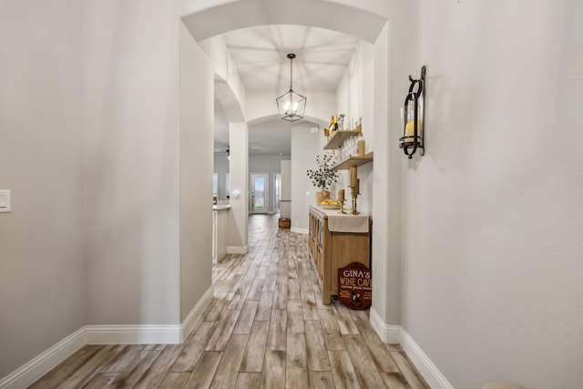 hallway featuring arched walkways, light wood-style flooring, and baseboards