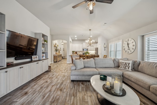 living area featuring arched walkways, lofted ceiling, visible vents, wood finished floors, and ceiling fan with notable chandelier