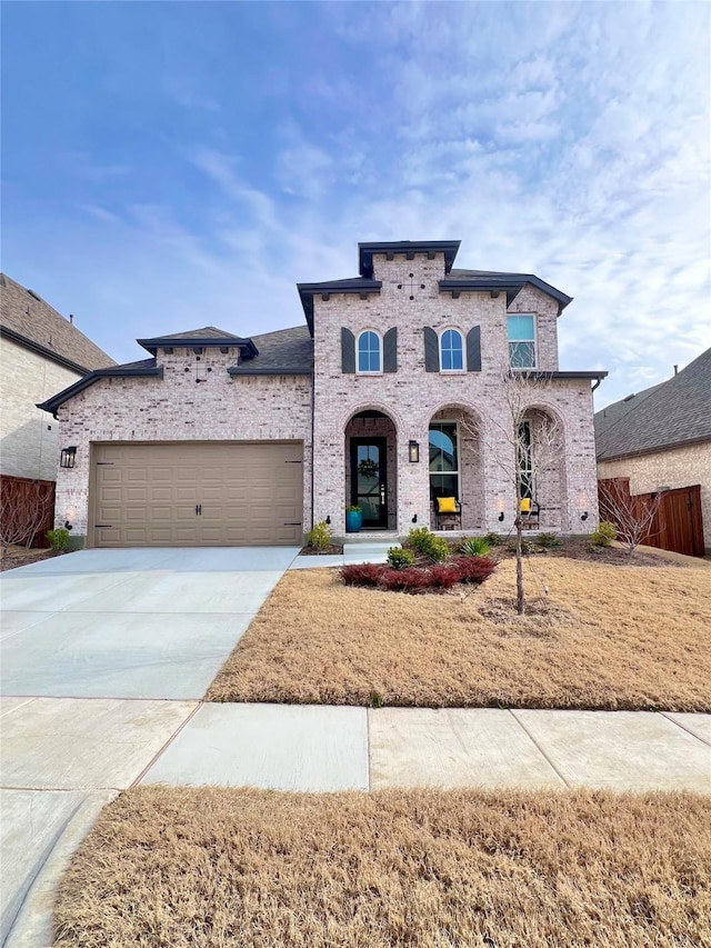 view of front of house with driveway, brick siding, an attached garage, and fence