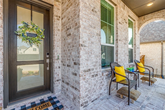 view of exterior entry featuring covered porch and brick siding