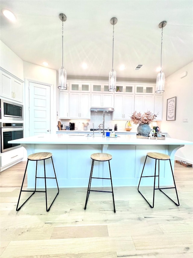 kitchen featuring oven, a breakfast bar, white cabinetry, light wood-style floors, and backsplash