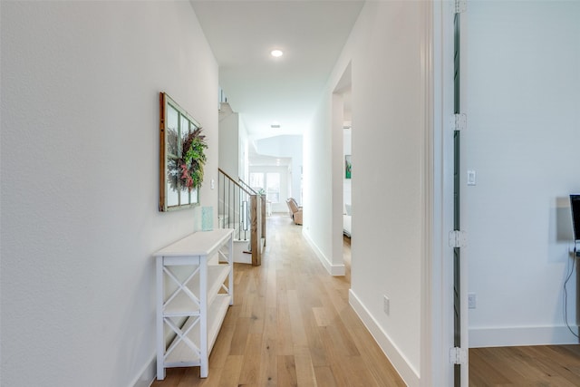 hallway with light wood finished floors, stairway, and baseboards