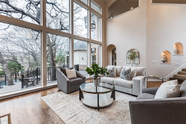 living room featuring stairway, a high ceiling, arched walkways, and wood finished floors