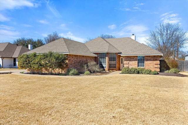 view of front of house featuring brick siding, a shingled roof, a chimney, and a front yard