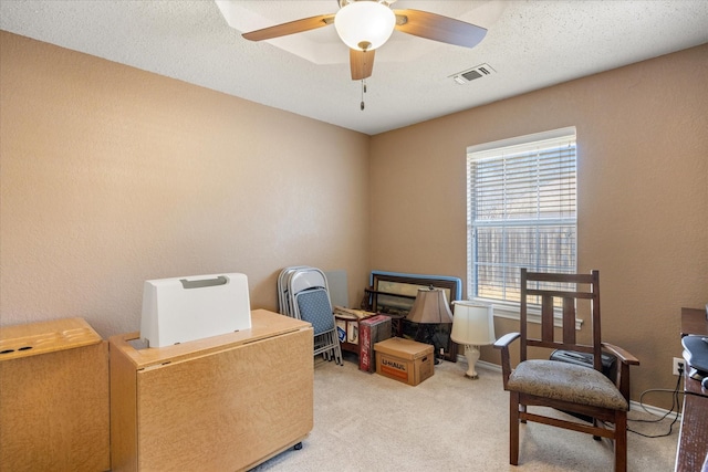 interior space featuring a textured ceiling, a ceiling fan, visible vents, and light colored carpet