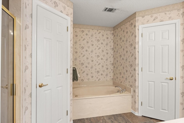 full bathroom with a textured ceiling, a garden tub, visible vents, a shower stall, and wallpapered walls