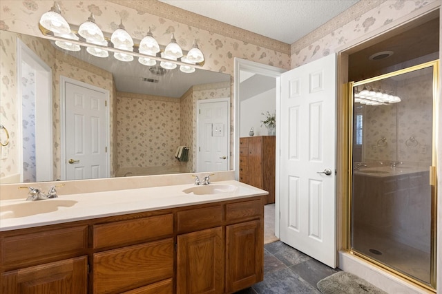 full bathroom featuring double vanity, wallpapered walls, a textured ceiling, a shower stall, and a sink