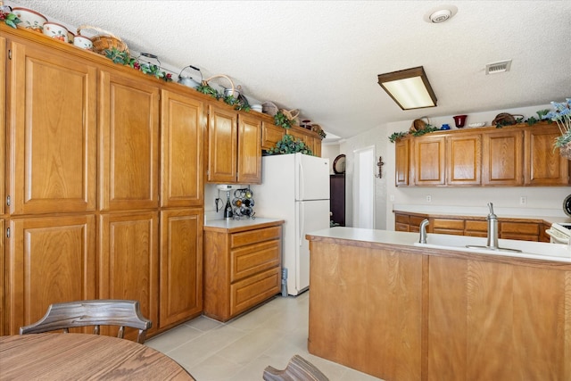 kitchen with visible vents, brown cabinetry, freestanding refrigerator, light countertops, and a textured ceiling