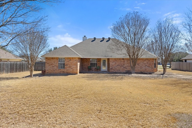 rear view of property featuring a yard, brick siding, fence, and a chimney