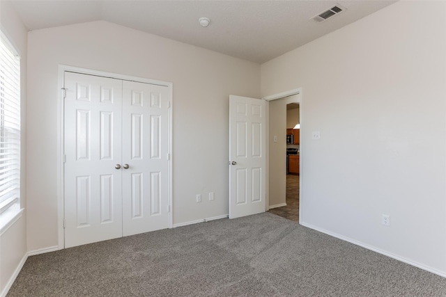 unfurnished bedroom with carpet, a closet, visible vents, and vaulted ceiling