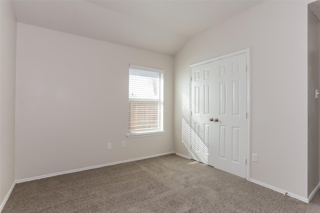 unfurnished bedroom featuring lofted ceiling, a closet, baseboards, and carpet flooring