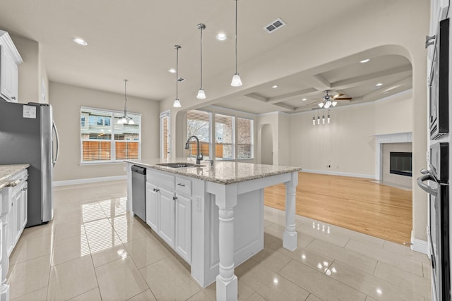 kitchen featuring a fireplace with flush hearth, light tile patterned floors, arched walkways, stainless steel appliances, and a sink