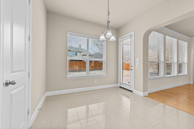 spare room featuring tile patterned floors, baseboards, and arched walkways