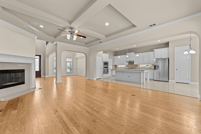 unfurnished living room featuring visible vents, light wood-style flooring, arched walkways, coffered ceiling, and a ceiling fan