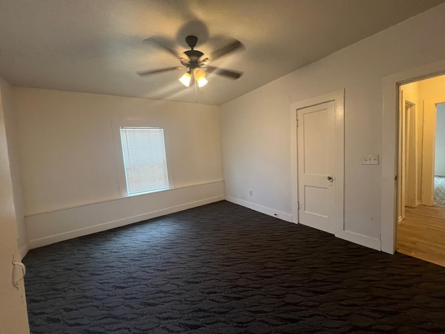 unfurnished room with ceiling fan, dark carpet, and baseboards